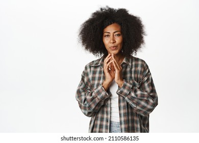 Cunning african american woman has plan, scheming, steeple fingers and smirking devious, has an idea, thinking smth interesting, standing over white background