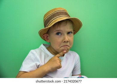 Cunning Child Boy In White T-shirt And Straw Hat Thinking On Green Background