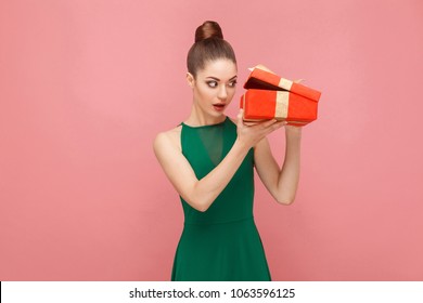 Cunning Woman Unboxing Red Gift Box Looking Inside. Expression Emotion And Feelings Concept. Studio Shot, Isolated On Pink Background