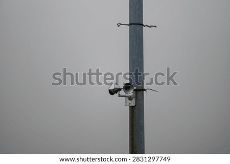 Cup anemometer wind speed sensor mounted on a metal pole against an overcast sky.
