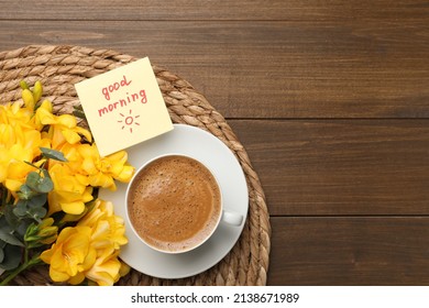 Cup of aromatic coffee, beautiful yellow freesias and Good Morning note on wooden table, flat lay. Space for text