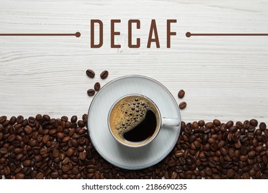 Cup of aromatic decaf coffee and beans on white wooden table, flat lay