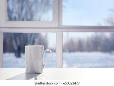 Cup Of Aromatic Tea On Windowsill. View Of Snowy Forest From Window