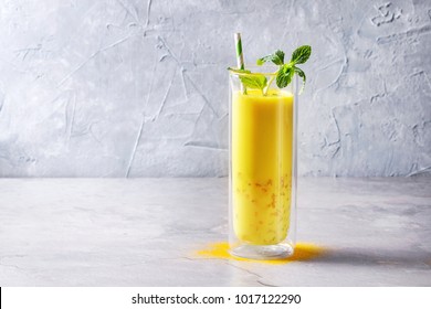 Cup of ayurvedic drink golden coconut milk turmeric iced latte with curcuma powder, crushed ice, mint over grey kitchen table. Copy space