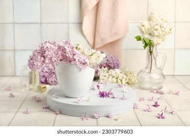 Cup of beautiful fragrant lilac flowers on stand near white tile