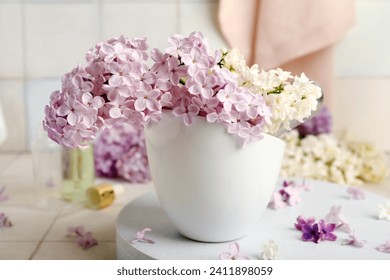 Cup of beautiful fragrant lilac flowers on stand near white tile