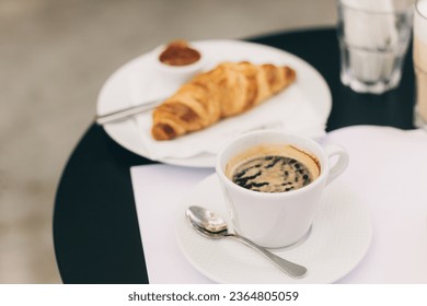 Cup of black coffee and a croissant on a table in a street cafe. Selective focus. Place for text. - Shutterstock ID 2364805059