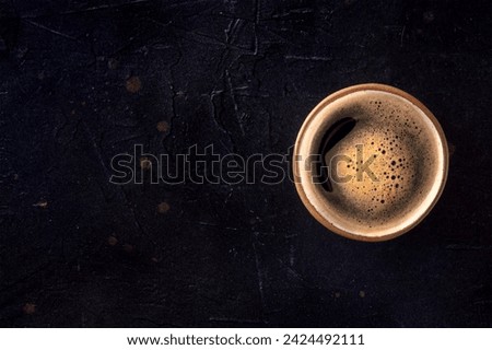 A cup of black coffee with froth, overhead flat lay shot on a black background, with copy space