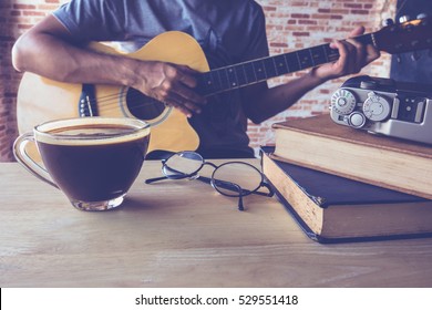 Cup Of Black Coffee On Table With A Man Play Guitar