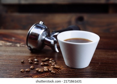 A cup of black coffee, roasted coffee beans and an espresso machine holder on a dark background.