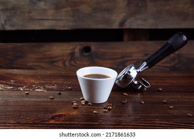 A cup of black coffee, roasted coffee beans and an espresso machine holder on a dark background.