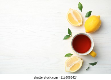 Cup of black tea and lemons on wooden table, top view