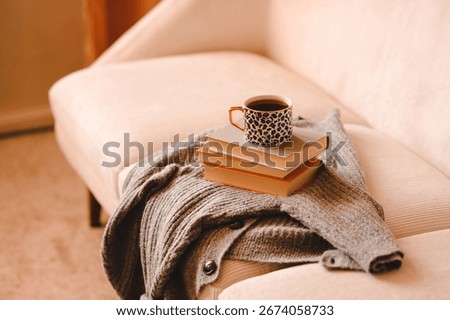 Cup of black tea on stack of paper books and knitted sweater cloth on couch in living room close up. Cozy home atmosphere. 