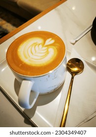 Cup of cafelatte, hot cafelatte with brass teaspoon, hot latte on table, latte art