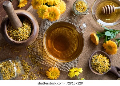 A cup of calendula (marigold) tea on a table, with fresh and dry calendula flowers in the background