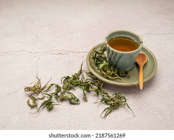 A cup of cannabis herbal tea with dry cannabis leaves on a table. Textured marijuana leaves. Concept of beverage with cannabis herb
