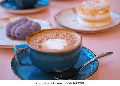 Cup of Cappuccino with Art Milk Foam Top View. Latte with Steel Spoon. Hot Coffee in a Blue Ceramic Mug With Saucer on a Pink Table. Modern Glamour Coffee Shop, Cafeteria. Thick Froth. No People. 4K