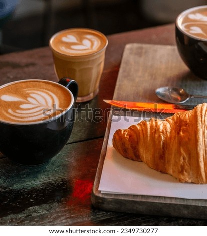 Cup of Cappuccino with beautiful cream latte art and a croissant on the side on a coffee shop table. Side view. Black Background.