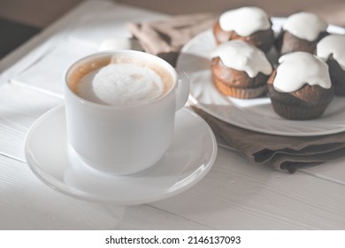 cup of cappuccino and chocolate muffins on white wooden cafe table. morning light. good morning concept. capuccino frost on a coffee