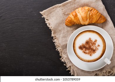 Cup Of Cappuccino Coffee And Croissant On Dark Table, Top View