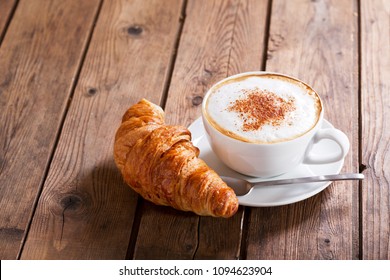 Cup Of Cappuccino Coffee With Croissant On Wooden Table