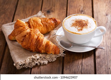 cup of cappuccino coffee with croissants on wooden table