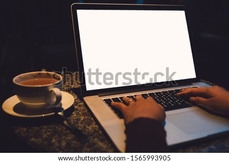Photo of A cup of cappuccino coffee with laptop white screen on table. Royalty high quality free stock photo image of coffee cup with laptop for working in a coffee shop, typing with blank screen white color