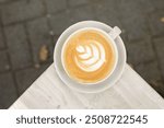 A cup of cappuccino coffee with milk on a saucer on the table outside on a cafe terrace, lifestyle horizontal top view photo with copy space