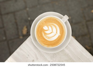 A cup of cappuccino coffee with milk on a saucer on the table outside on a cafe terrace, lifestyle horizontal top view photo with copy space