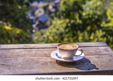 Cup of cappuccino coffee on wooden table bokeh annd blur village background