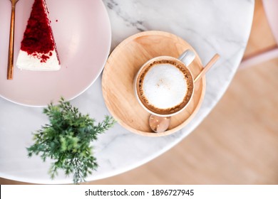 Cup Of Cappuccino Coffee And Red Velvet Sweet Cake On Table In Beautiful Cafe. Cappuccino Coffee Often Served With Sweet Cake In Cafe And Restaurant. Cup Of Cappuccino Coffee In Cute Cafe Concept. 