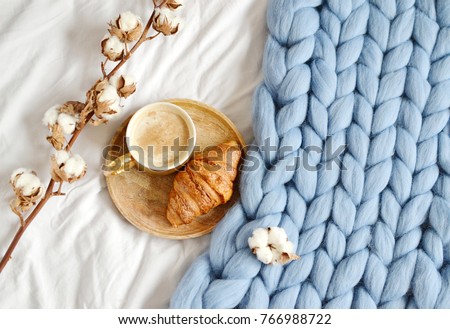 Cup with cappuccino, croissant, blue pastel giant plaid, bedroom, morning concept, cotton flower top view