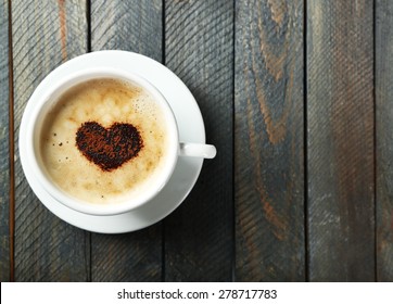 Cup of cappuccino with heart of cocoa on wooden table