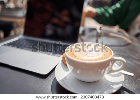 A cup of cappuccino and a laptop on the table in a coffee shop. Workplace in a coffee shop in the morning. coffee break.
