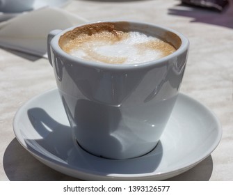 A cup of cappuccino on a sunny day, on a table in a street cafe.