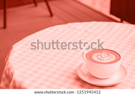 A cup of cappuccino on a table with a checkered tablecloth.