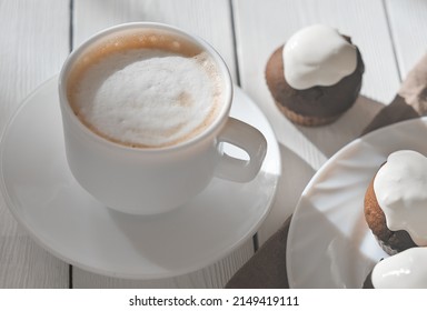a cup of capuccino and mini cakes with icing. natural light, morning time. breakfast for family weekend or coffee break