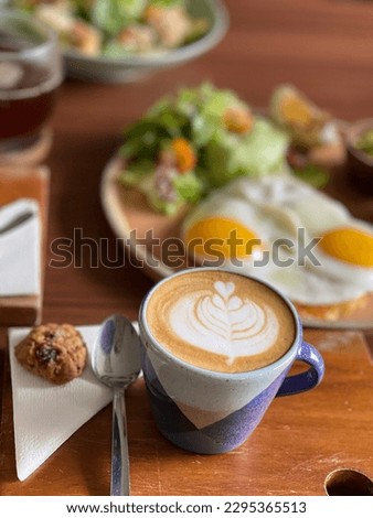 A cup of capucinno with latte art, accompanied by typical american breakfast
