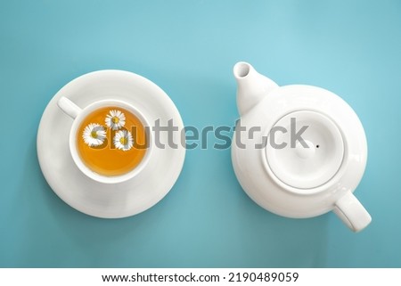A cup of chamomile tea and a teapot on a blue background.