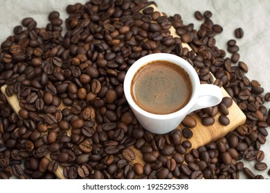 A cup of coffee among selected and calibrated Arabica coffee beans scattered on a napkin, table, blended, top view