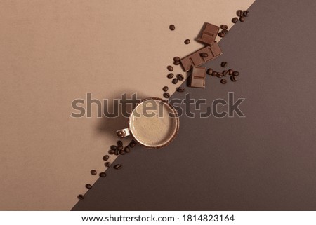 A cup of coffee, coffee beans and chocolate pieces top view over modern brown background. 