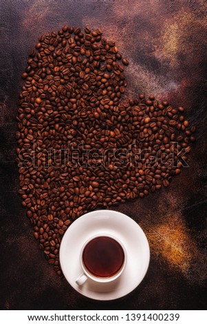 A cup of coffee and coffee beans poured in the form of a heart, top view
