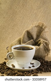 Cup of coffee with beans and sack over brown burlap background
