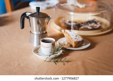 Cup of coffee with beautiful butter cake, rosemary branch and tradutional italian geyser coffee maker. Selective focus.