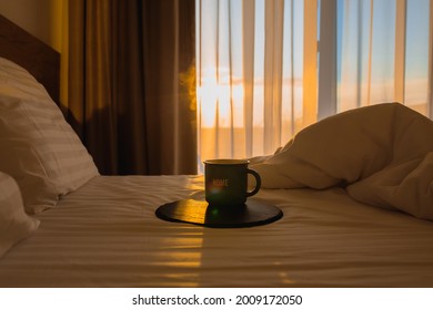 Cup of coffee in bed at sunrise. Dawn with a cup of coffee in bed. Hot coffee in bed. Waking up with hot coffee in a white bed. The sun shines into the bedroom in the morning. A beautiful morning.