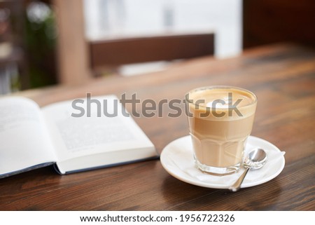 Cup of coffee and book on the table in street cafe. Cappuccino or latte in glass. Enjoying time alone