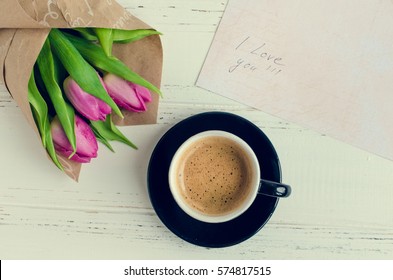 Cup of coffee with bouquet of pink tulips and notes I LOVE YOU on white shabby chic background with place for text. Romantic Valentines concept. Valentine's day greeting card. Top view. Copy space.