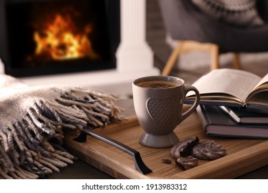 Cup of coffee, broken cookie and books on wooden table near fireplace indoors. Cozy atmosphere - Powered by Shutterstock