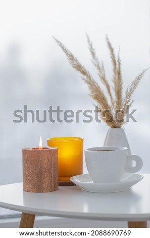 cup of coffee with burning candles  on white table by window on winter