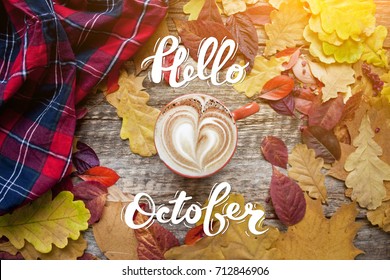 A cup of coffee with cappuccino and autumn leaves on old wooden background with hand lettering Hello October. Autumn decor, fall mood, autumn still life.